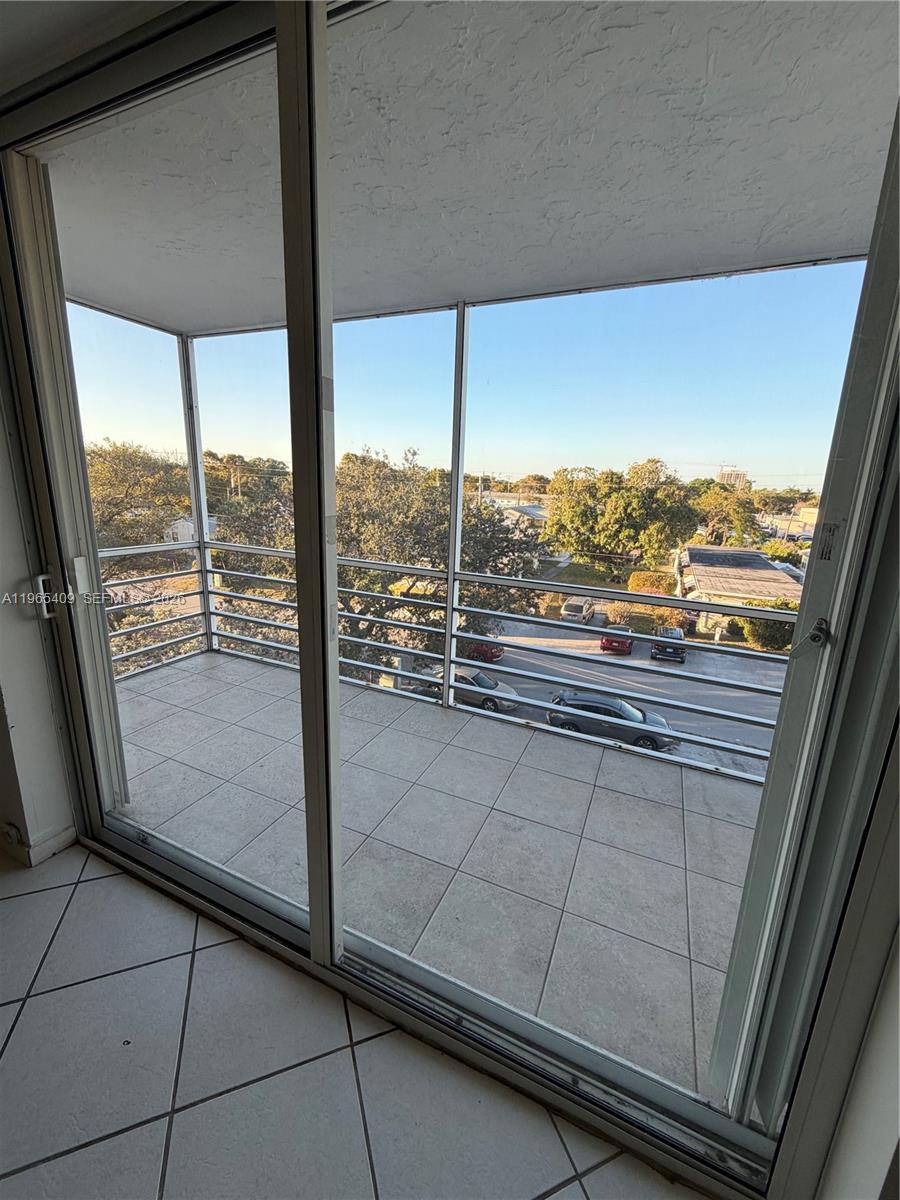 A tiled balcony with a metal railing overlooks a street with parked cars and trees — 1830 Dixieanna St # 406, Hollywood FL 33020, HOLLYWOOD, FL