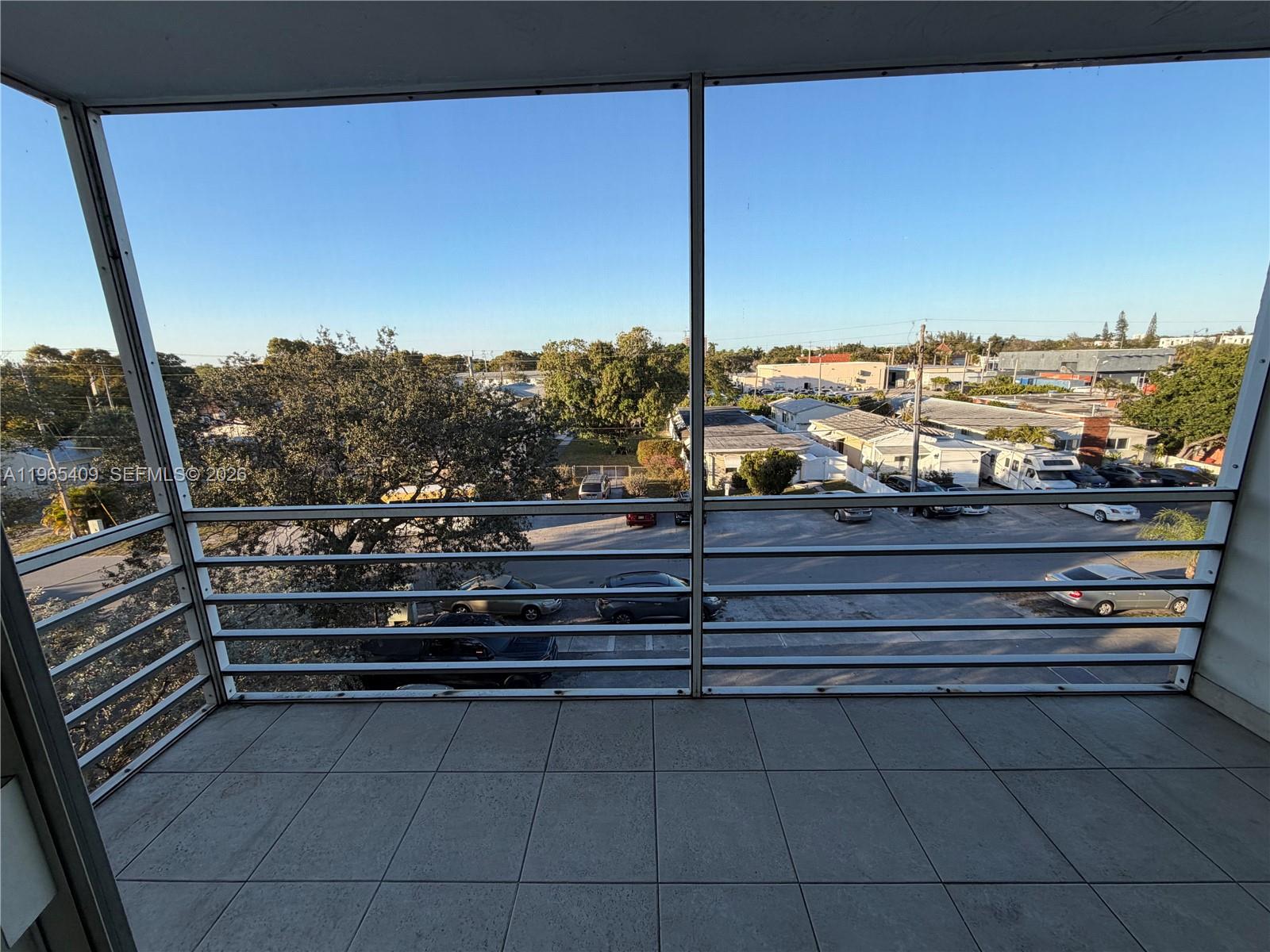 A tiled balcony with a metal railing overlooks a parking lot and neighborhood buildings — 1830 Dixieanna St # 406, Hollywood FL 33020, HOLLYWOOD, FL