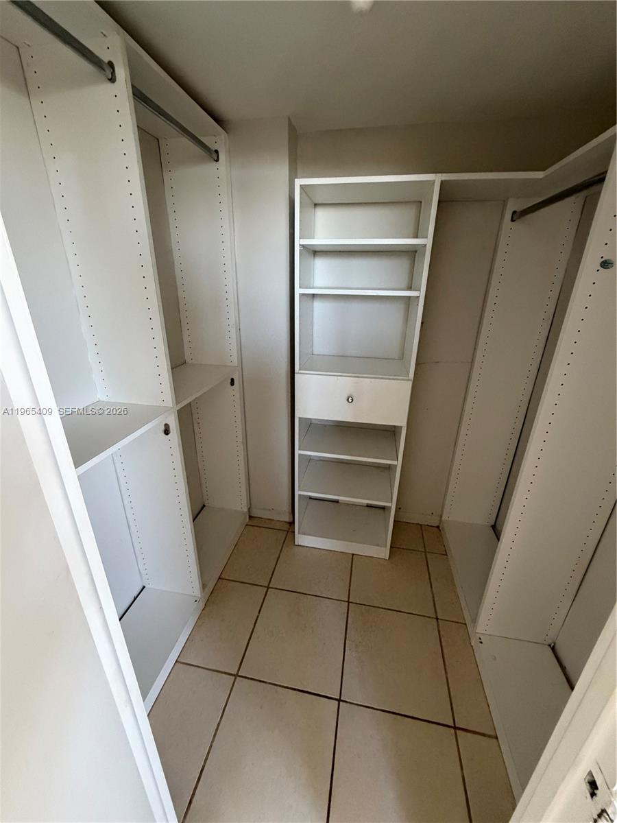 A walk-in closet features white shelving units, hanging rods, and light-colored tile flooring — 1830 Dixieanna St # 406, Hollywood FL 33020, HOLLYWOOD, FL