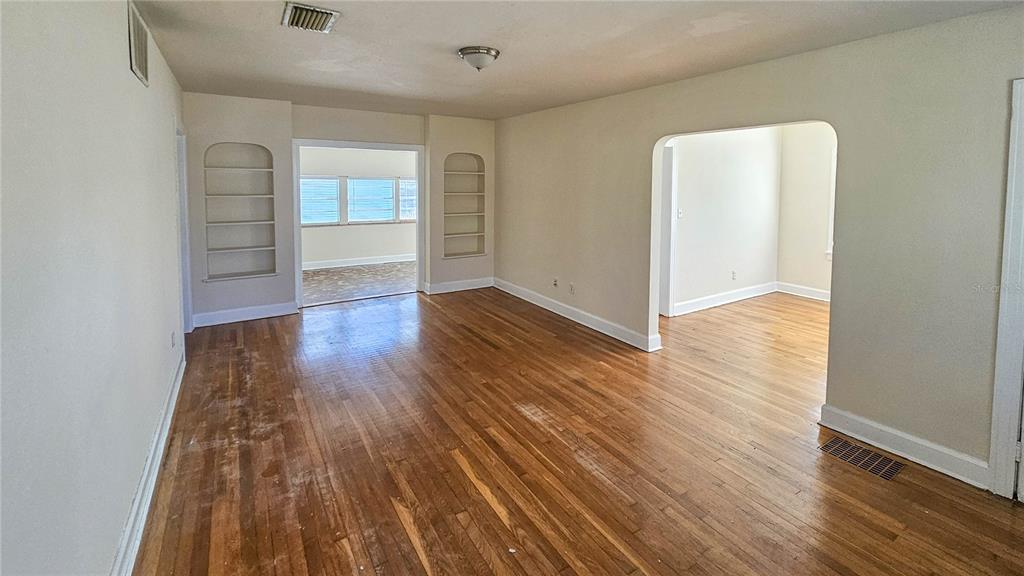An empty living room features hardwood floors, built-in shelving, and arched doorways leading to other rooms — 860 16TH AVENUE S, ST PETERSBURG, FL