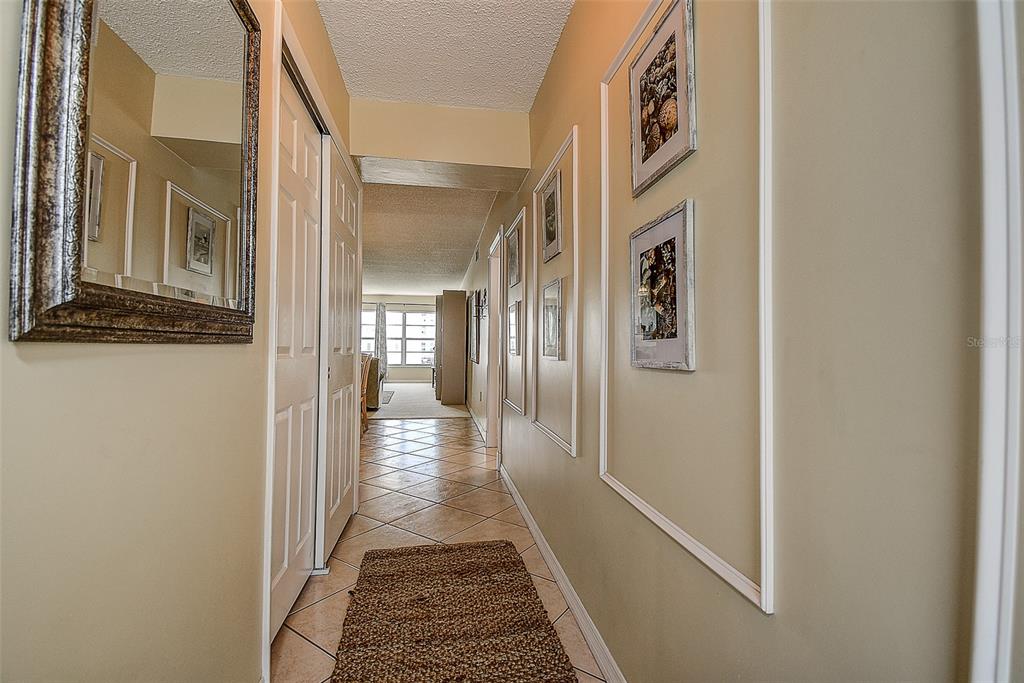 A hallway with tile flooring, a mirror, framed wall art, and a view into a room — 6363 GULF WINDS DRIVE UNIT 327, ST PETE BEACH, FL