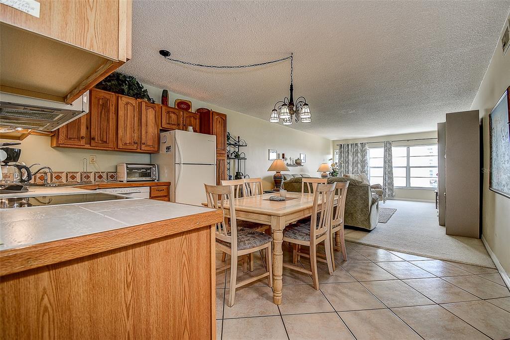 A kitchen with wood cabinets and tile floors opens to a dining area and living room — 6363 GULF WINDS DRIVE UNIT 327, ST PETE BEACH, FL