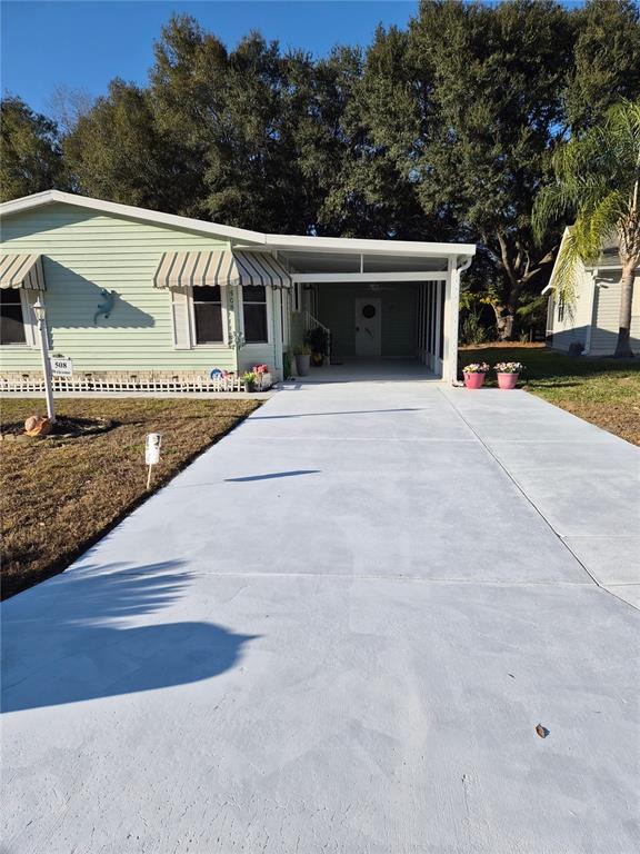 A light green manufactured home features a covered carport and a freshly painted concrete driveway — 508 SAINT ANDREWS BOULEVARD, LADY LAKE, FL