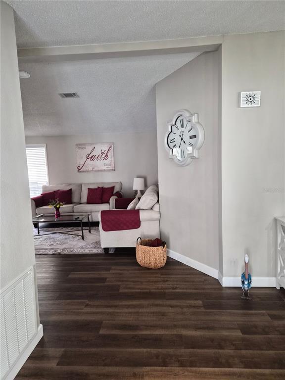 A living room features dark wood-look flooring, a beige sofa, and a decorative wall clock — 508 SAINT ANDREWS BOULEVARD, LADY LAKE, FL