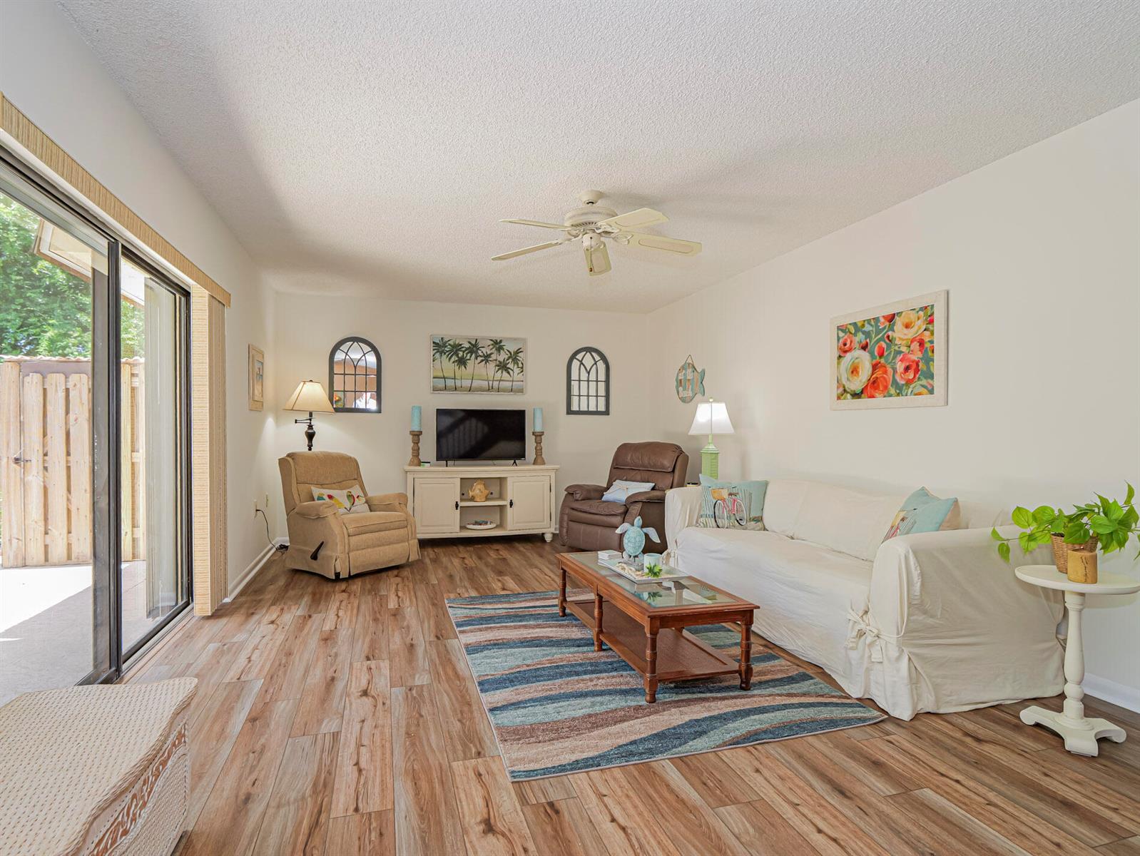 A living room features wood-look flooring, a white sofa, two recliners, and a television console — 340 S Waverly Place # 8b, Vero Beach FL 32960, VERO BEACH, FL