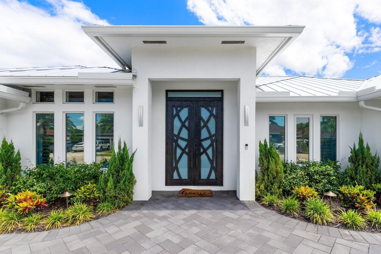 A modern white house exterior features a dark double door entrance and a paved walkway — 11164 Boca Woods Lane, Boca Raton FL 33428, BOCA RATON, FL
