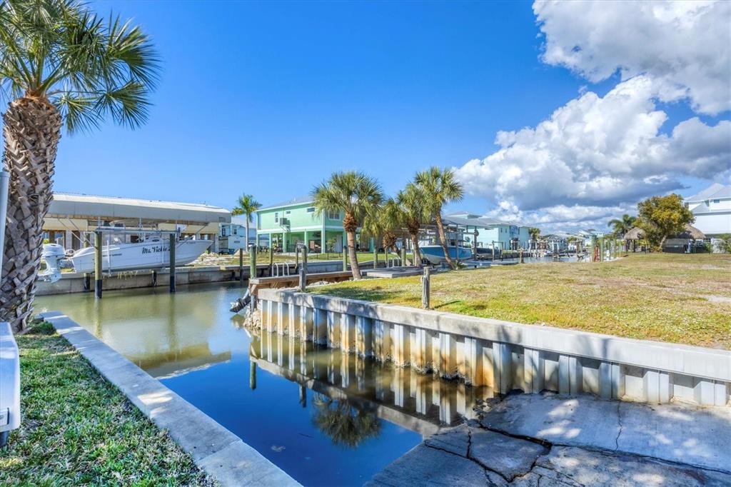 A canal-front lot features a concrete seawall, a boat lift, and several palm trees — 10484 RAYMOND STREET, ENGLEWOOD, FL