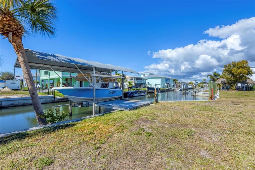 A boat on a lift sits in a canal next to a grassy yard — 10484 RAYMOND STREET, ENGLEWOOD, FL