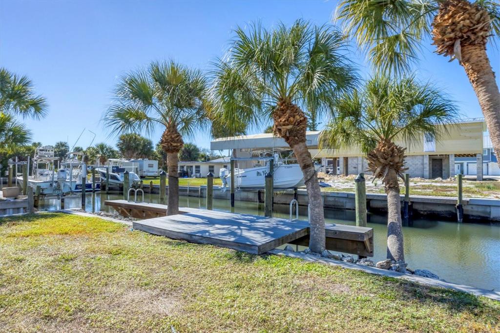 A wooden dock sits on a canal lined with palm trees and several moored boats — 10484 RAYMOND STREET, ENGLEWOOD, FL