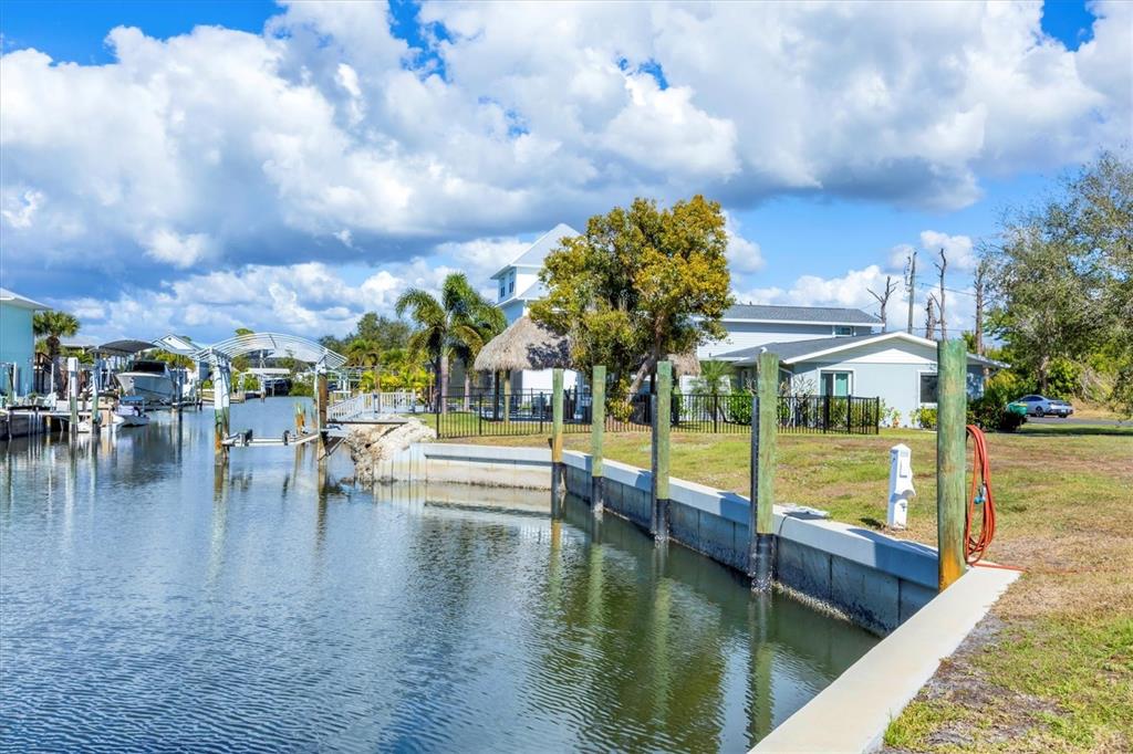 A canal-front property features a concrete seawall, wooden pilings, and a boat lift — 10484 RAYMOND STREET, ENGLEWOOD, FL