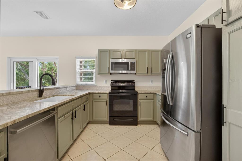 A kitchen features sage green cabinets, stainless steel appliances, and light-colored granite countertops — 307 SUMMER CLOUDS PLACE, BRANDON, FL