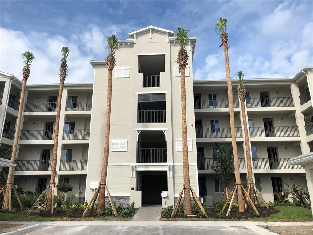 A multi-story apartment building exterior features balconies, palm trees, and a central stairwell entrance — 1010 TIDEWATER SHORES LOOP UNIT 206, BRADENTON, FL