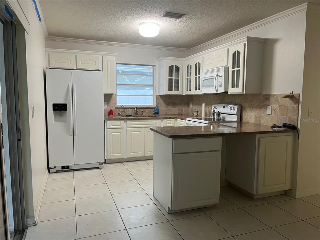 A kitchen features white cabinets, a white refrigerator, tiled countertops, and light-colored floor tiles — 3021 W TAMPA BAY BOULEVARD, TAMPA, FL
