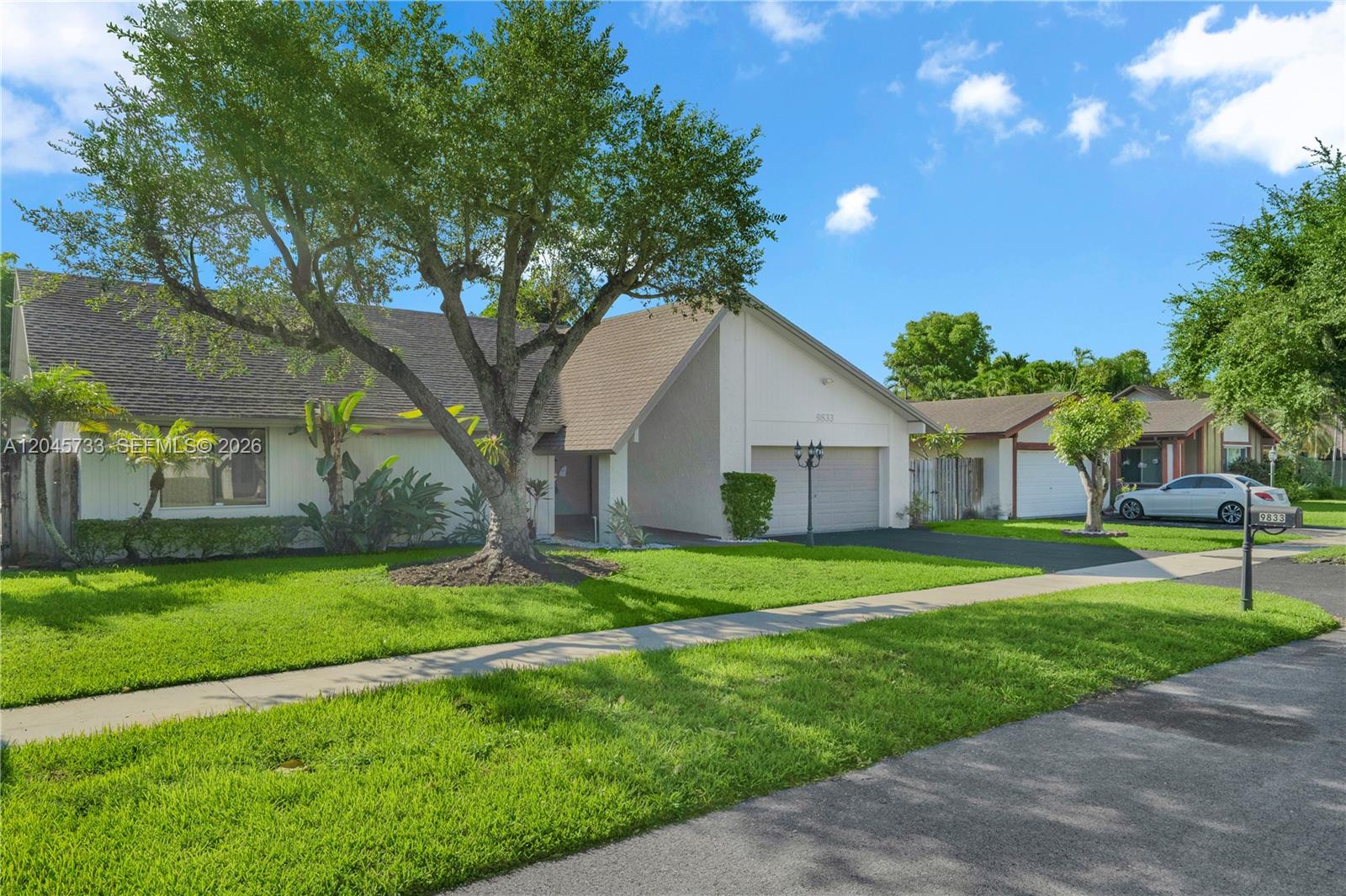 A single-story house with a large tree, a two-car garage, and a green lawn — MIAMI, FL