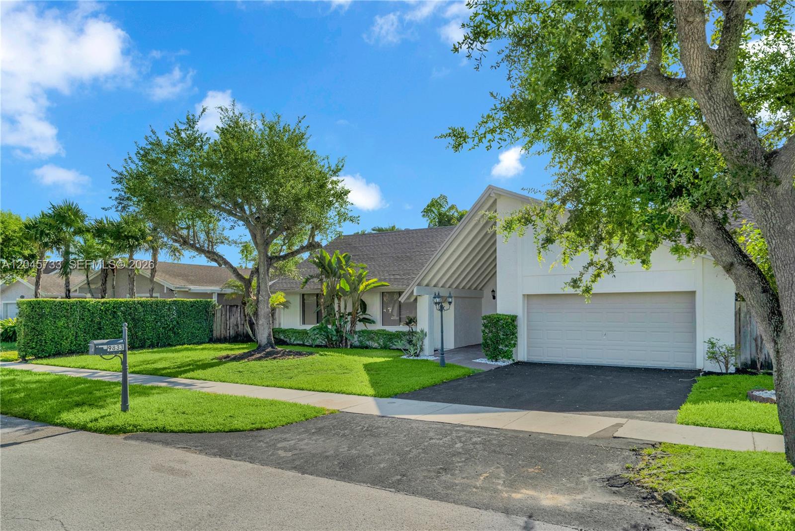 A single-story house with a white exterior, a two-car garage, and a large front tree — MIAMI, FL