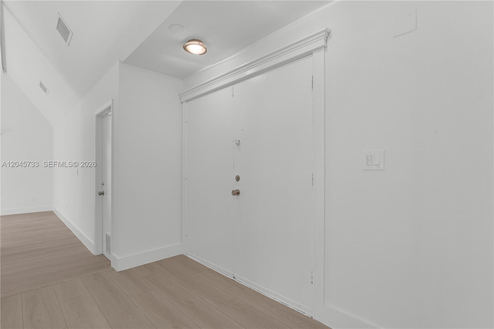 A white double door with a light fixture above sits in a room with wood-look flooring — MIAMI, FL