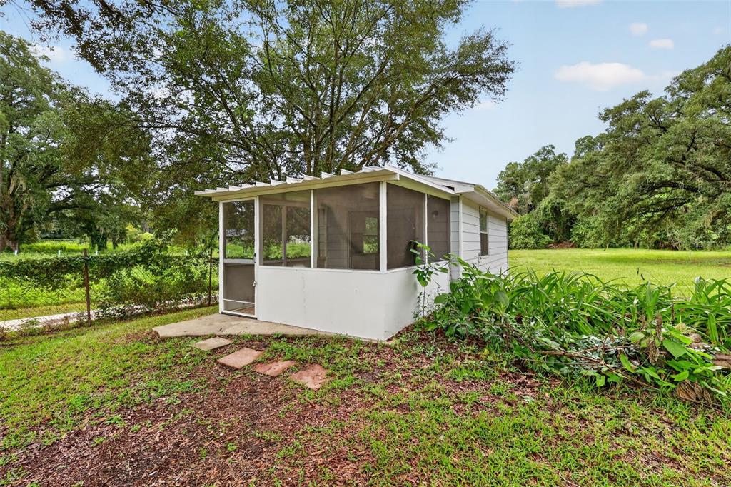 A small white screened-in porch sits on a grassy lawn under large shade trees — 2888 SE 59TH STREET, OCALA, FL