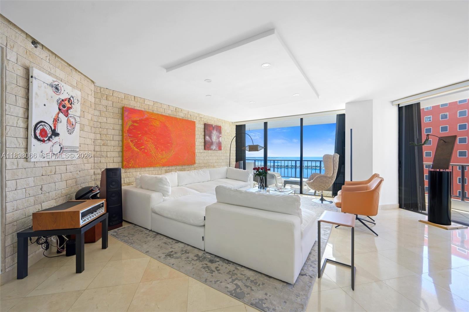 A living room features a white sectional sofa, stone accent wall, and floor-to-ceiling windows — 1581 Brickell Ave # 2005, Miami FL 33129, MIAMI, FL
