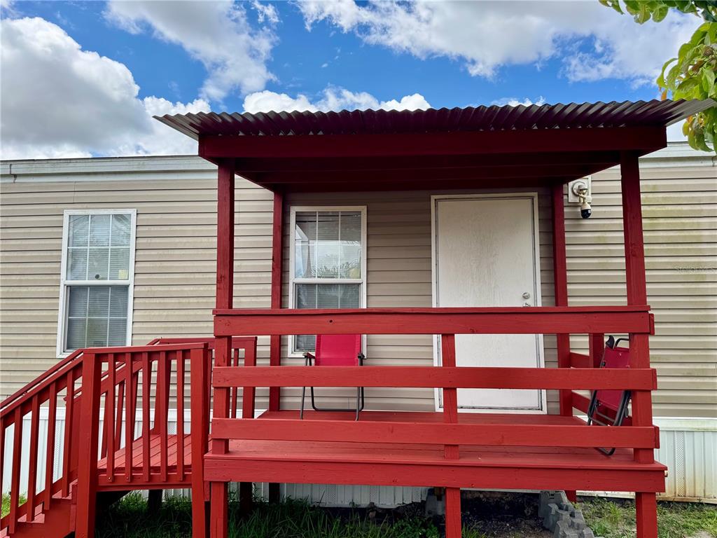 A red wooden porch with a metal roof is attached to a tan mobile home — 7515 RANCHERO STREET, ORLANDO, FL