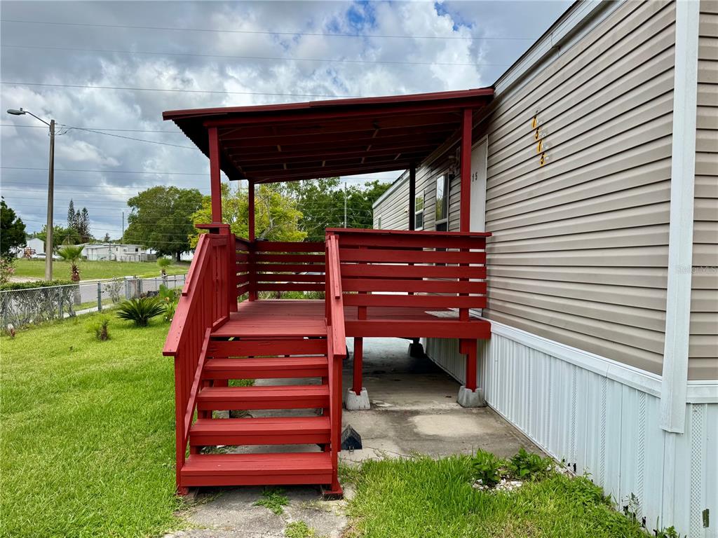A red wooden deck with stairs and a roof attached to a mobile home exterior — 7515 RANCHERO STREET, ORLANDO, FL