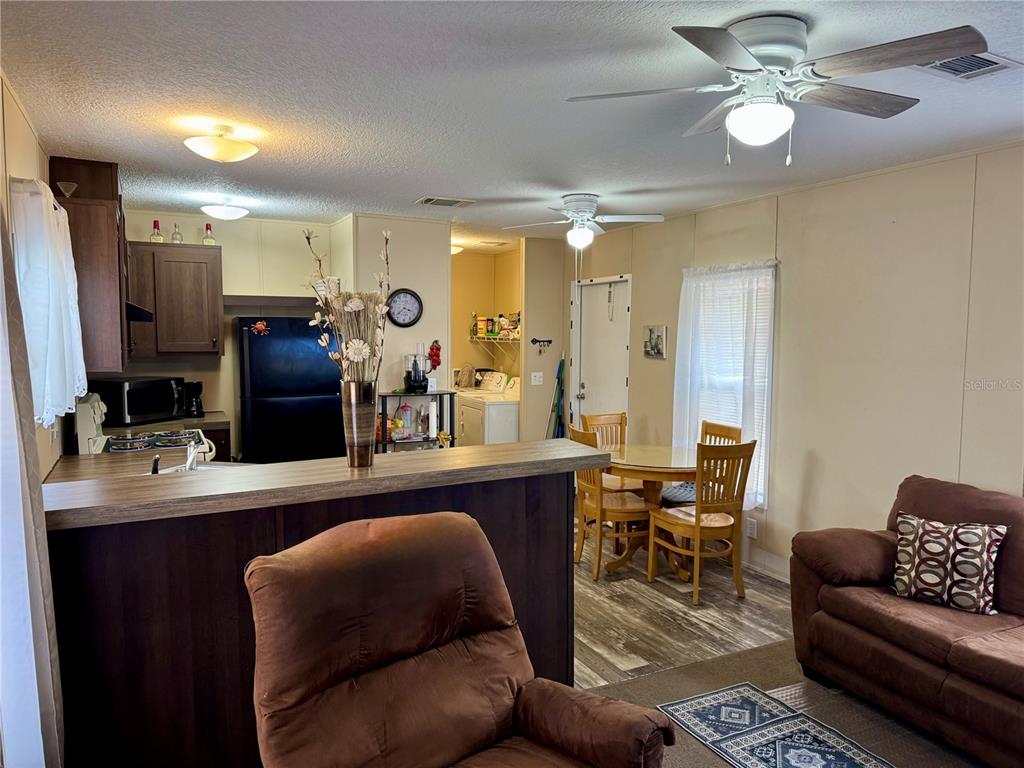 An open-concept living area features a kitchen with dark cabinets, a dining space, and furniture — 7515 RANCHERO STREET, ORLANDO, FL