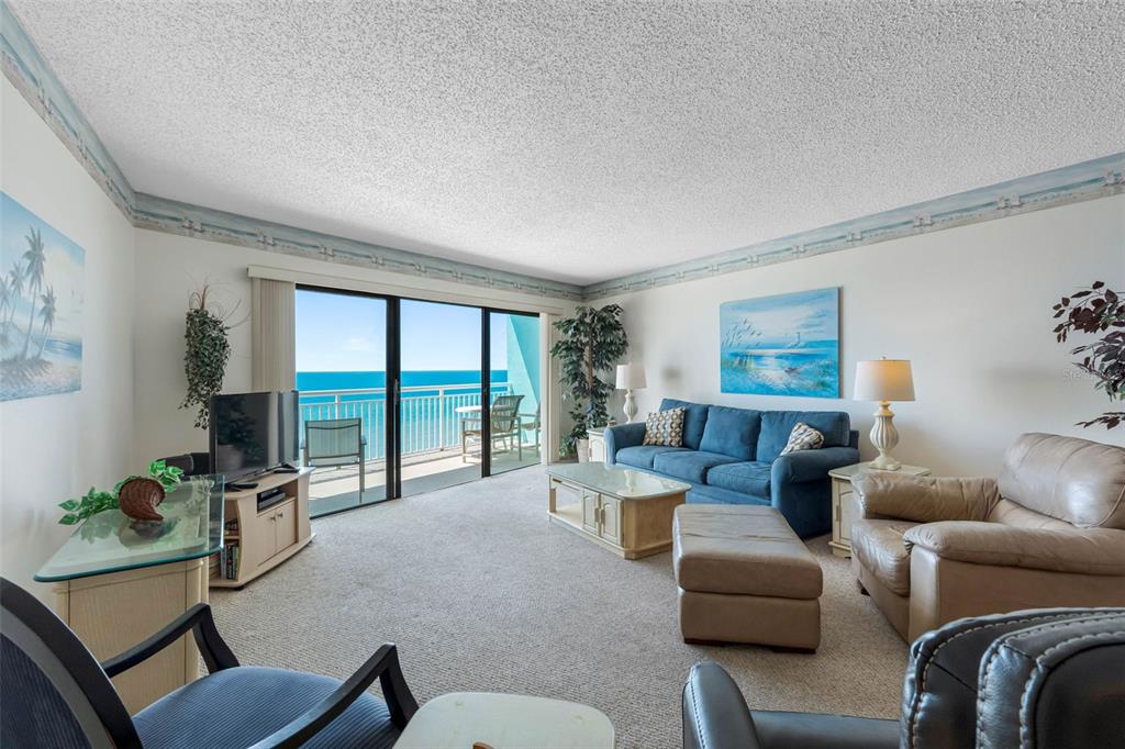 A living room features a blue sofa, beige armchair, and sliding glass doors overlooking the ocean — 19440 GULF BOULEVARD UNIT 506, INDIAN ROCKS BEACH, FL