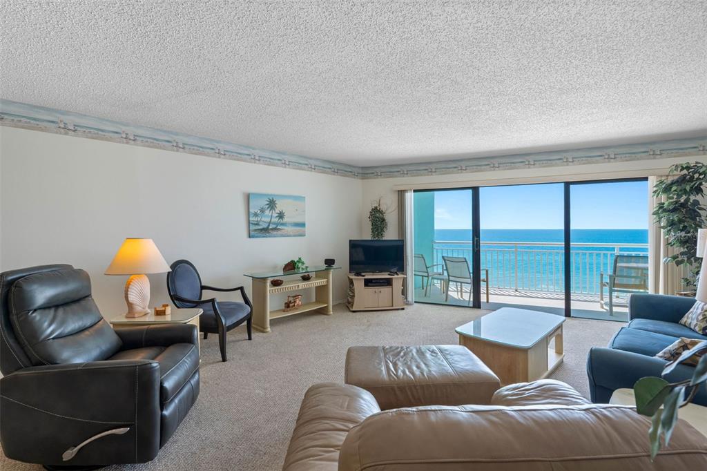 A living room with beige carpet, a leather recliner, and a balcony overlooking the ocean — 19440 GULF BOULEVARD UNIT 506, INDIAN ROCKS BEACH, FL