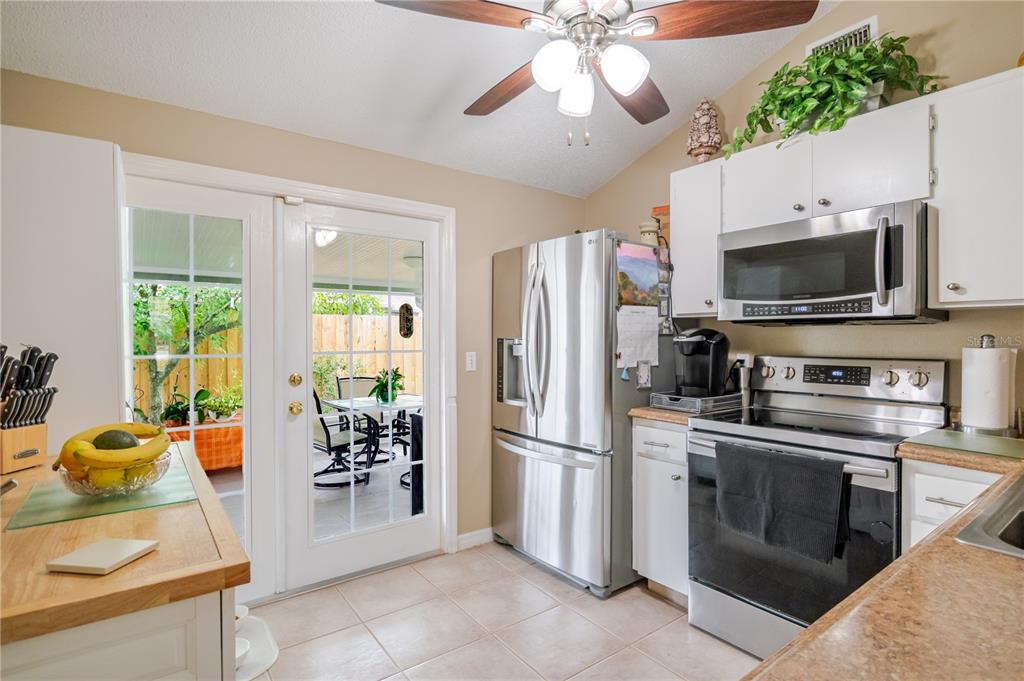 A kitchen features stainless steel appliances, white cabinets, a ceiling fan, and a glass-paned door — 10118 HUNTERS POINT COURT, TAMPA, FL
