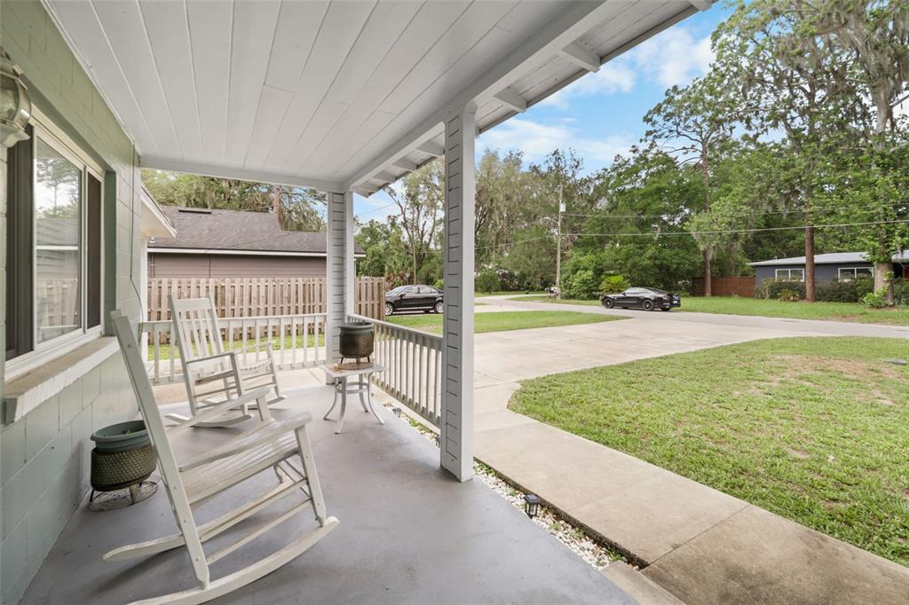 A covered front porch features two white rocking chairs, a small table, and a concrete floor — 4323 NW 12TH TERRACE, GAINESVILLE, FL