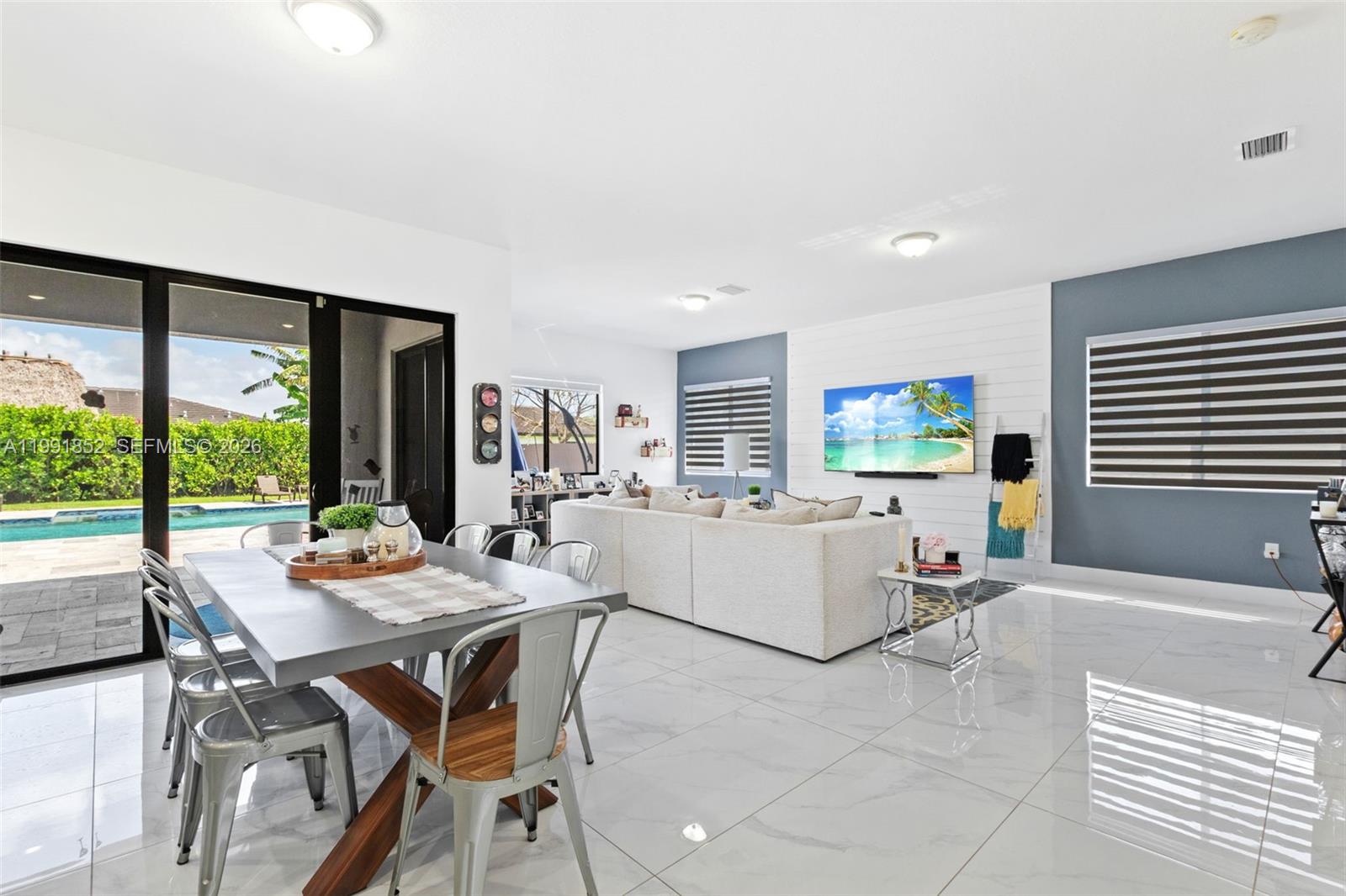 A bright open-concept living and dining area features white tile floors and a pool view — 13217 SW 227th St, Miami FL 33170, MIAMI, FL