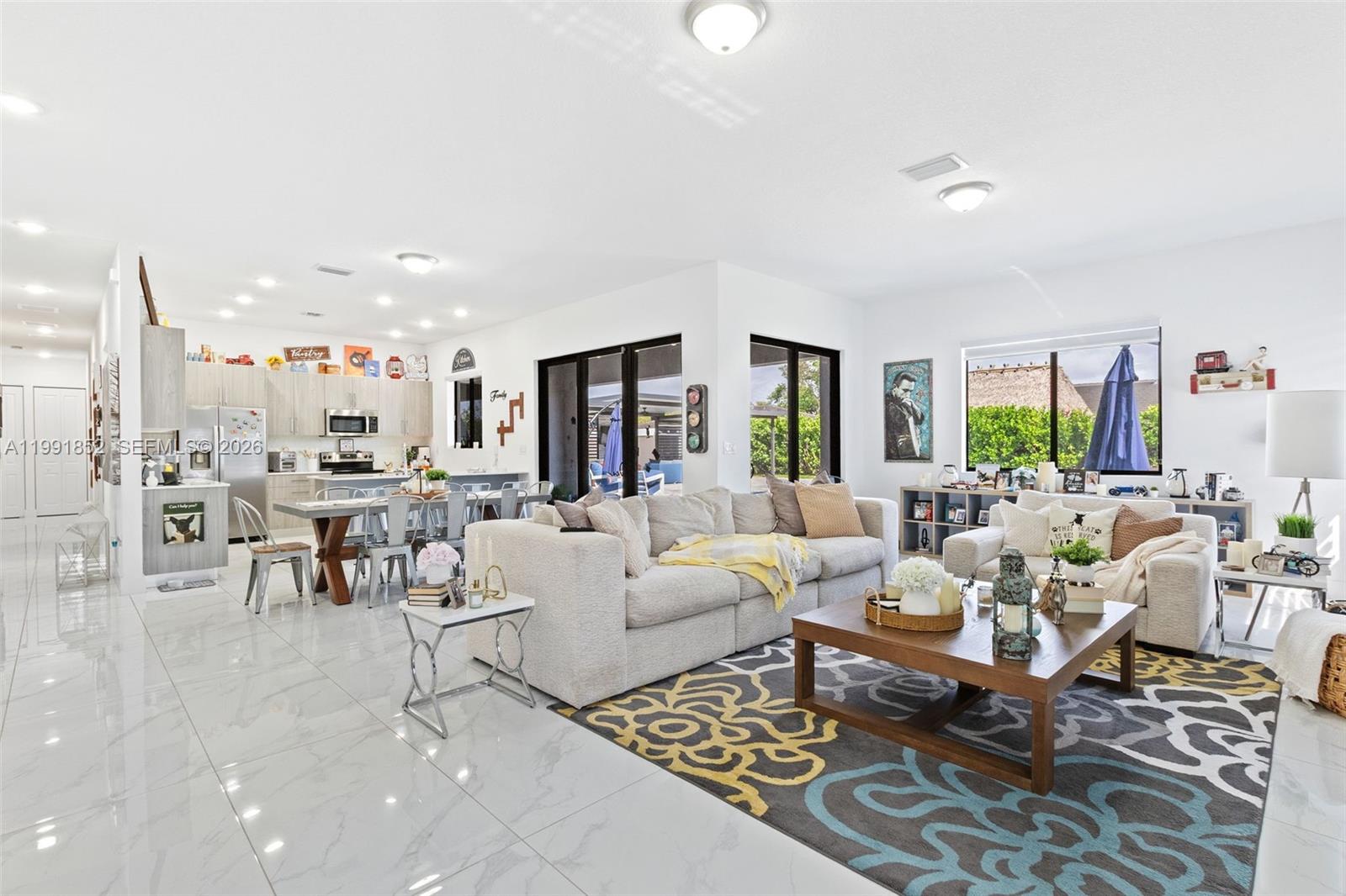 An open-concept living room and kitchen featuring white tile floors and a patterned area rug — 13217 SW 227th St, Miami FL 33170, MIAMI, FL