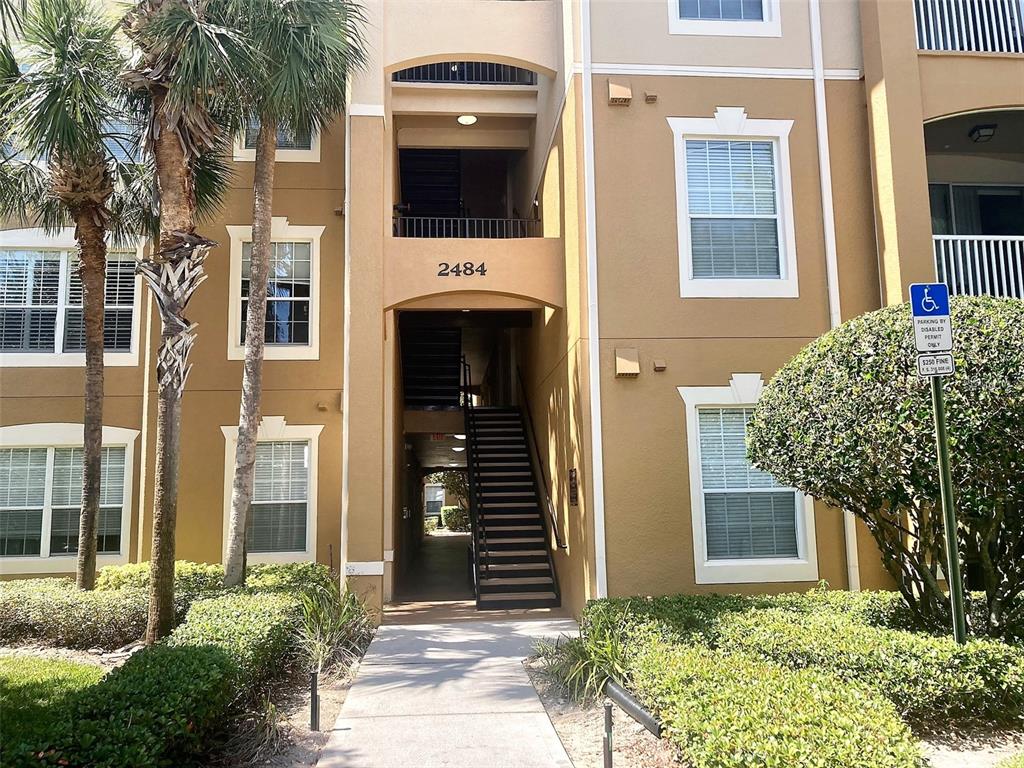 An exterior view of a multi-story apartment building with a central staircase and palm trees — 2484 SAN TECLA STREET UNIT 310, ORLANDO, FL