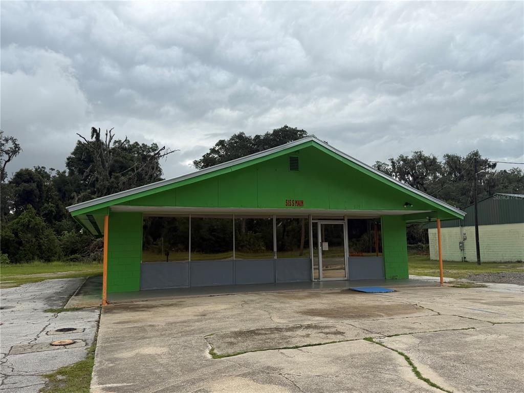 A bright green, single-story commercial building with a large glass storefront and concrete parking lot — 515 S MAIN STREET, CHIEFLAND, FL