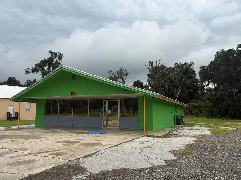 A bright green, single-story commercial building with a large glass storefront and concrete parking lot — 515 S MAIN STREET, CHIEFLAND, FL