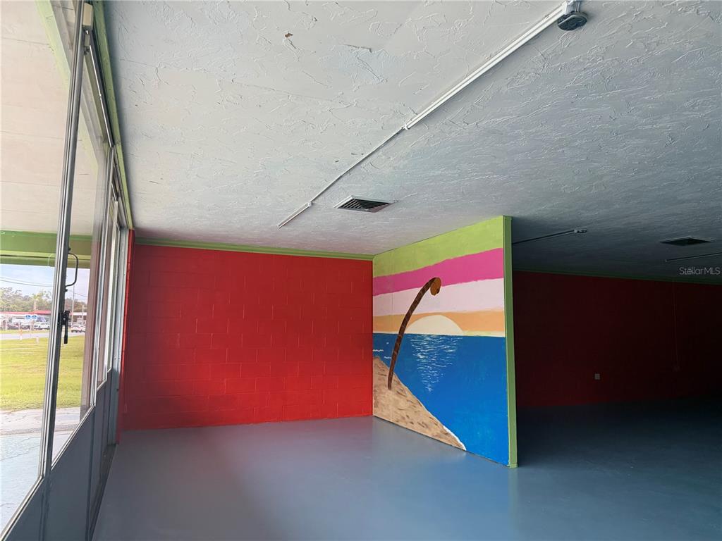 An interior space features a red block wall, a painted beach mural, and gray flooring — 515 S MAIN STREET, CHIEFLAND, FL