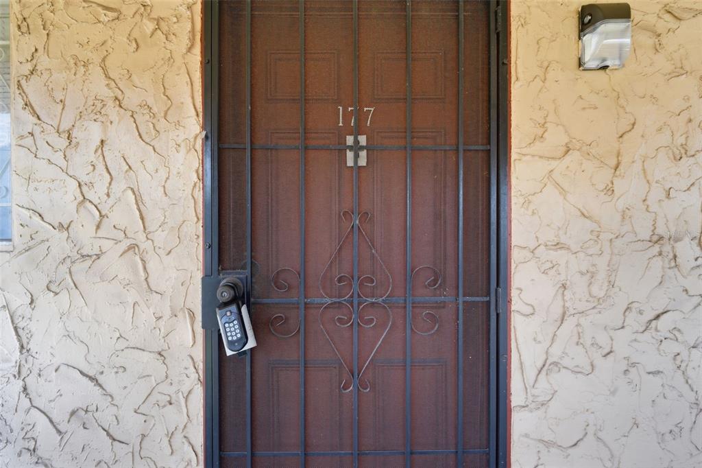 A brown door with a decorative metal security gate and a lockbox sits in a stucco wall — 2868 N POWERS DRIVE UNIT 177, ORLANDO, FL