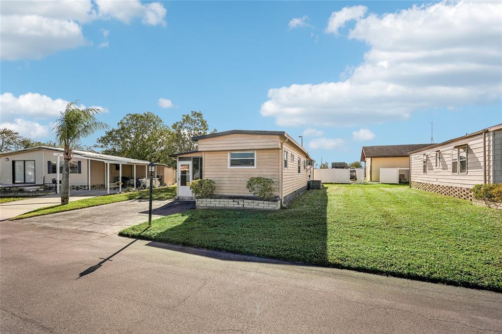 A single-story manufactured home with light-colored siding sits on a grassy lot near a street — 5316 53RD AVENUE E UNIT F43, BRADENTON, FL
