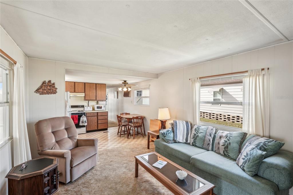 A living room with carpeted floors and a sofa leads into a kitchen with dining area — 5316 53RD AVENUE E UNIT F43, BRADENTON, FL