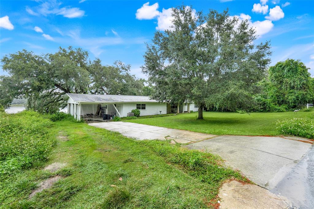 A white single-story house with a carport sits on a grassy lot with large trees — 1148 PEARL VIEW DRIVE, ALTAMONTE SPRINGS, FL