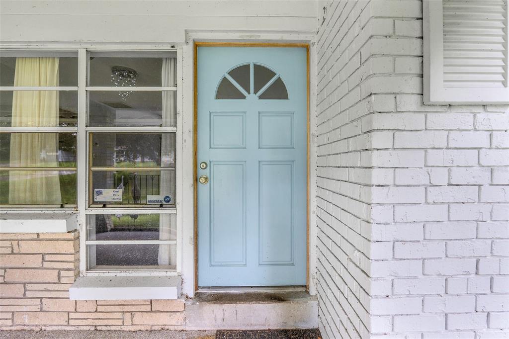 A light blue front door sits beside a large window and a white brick wall — 1148 PEARL VIEW DRIVE, ALTAMONTE SPRINGS, FL