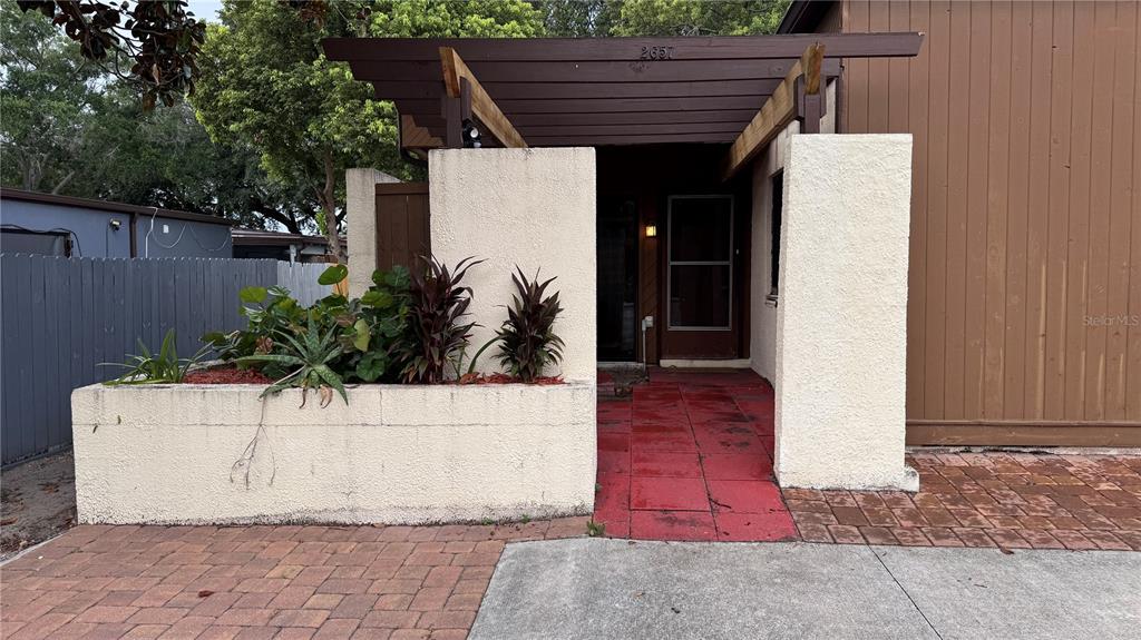 The exterior entrance features a red tiled walkway, a wooden pergola, and a stucco planter — 2657 EXUMA WAY, WINTER PARK, FL