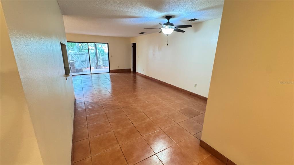 An empty living room features brown tile flooring, a ceiling fan, and sliding glass doors — 2657 EXUMA WAY, WINTER PARK, FL