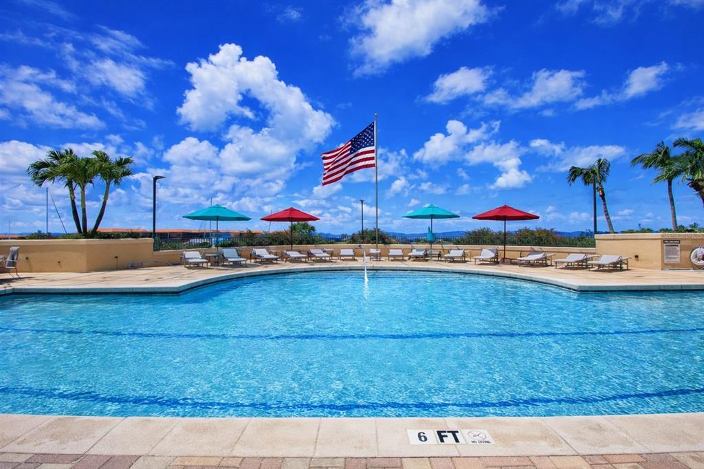 A swimming pool with lounge chairs, colorful umbrellas, and an American flag under a blue sky — 3321 SUNSET KEY CIRCLE UNIT 502, PUNTA GORDA, FL