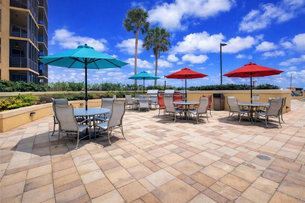 An outdoor patio features several dining tables with umbrellas and chairs on a paved deck — 3321 SUNSET KEY CIRCLE UNIT 502, PUNTA GORDA, FL