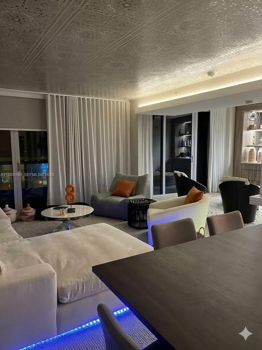A modern living room features a wall-mounted television, neutral furniture, and an open bar area — 9401 Collins Ave # 305, Surfside FL 33154, SURFSIDE, FL