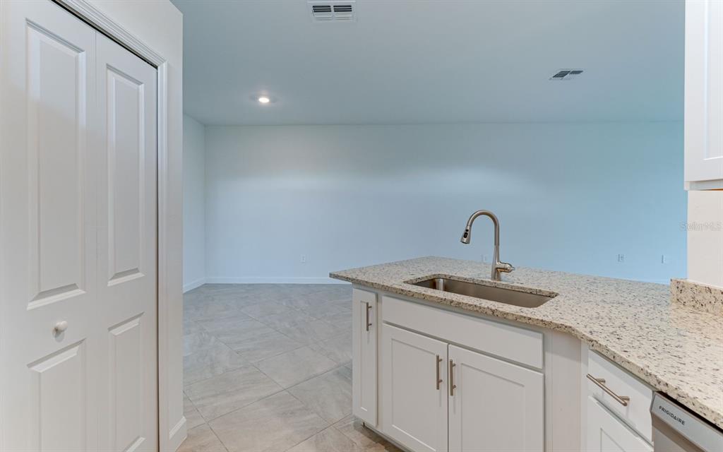 A kitchen island with a stainless steel sink and granite countertop overlooks an empty room — 5343 WHITE SAND COVE, BRADENTON, FL