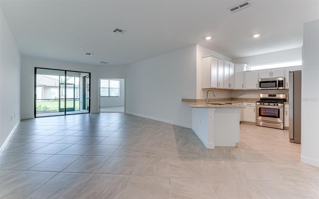 An open-concept kitchen with white cabinets and granite countertops overlooks a tiled living area — 5343 WHITE SAND COVE, BRADENTON, FL