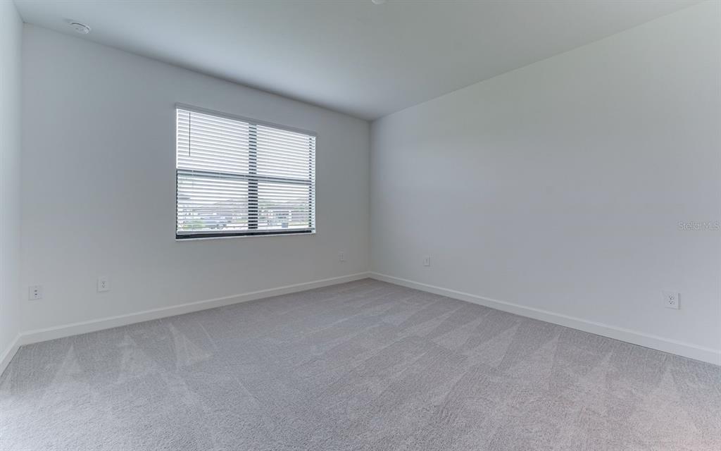 An empty bedroom features white walls, gray carpeting, and a window with white blinds — 5343 WHITE SAND COVE, BRADENTON, FL