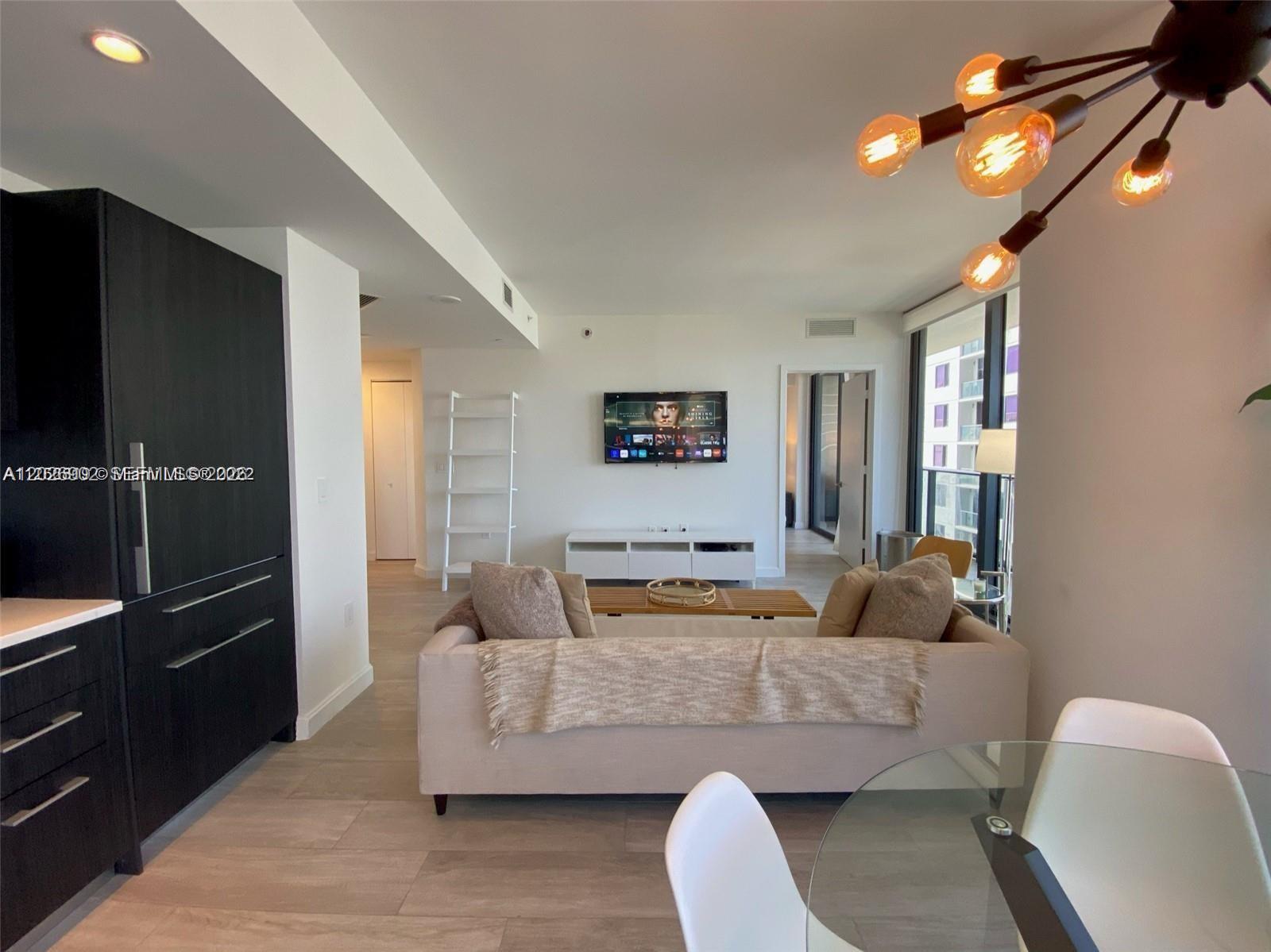 A modern living room features a sofa, television, and dining area with light wood flooring — 55 SW 9th St # 3001, Miami FL 33130, MIAMI, FL