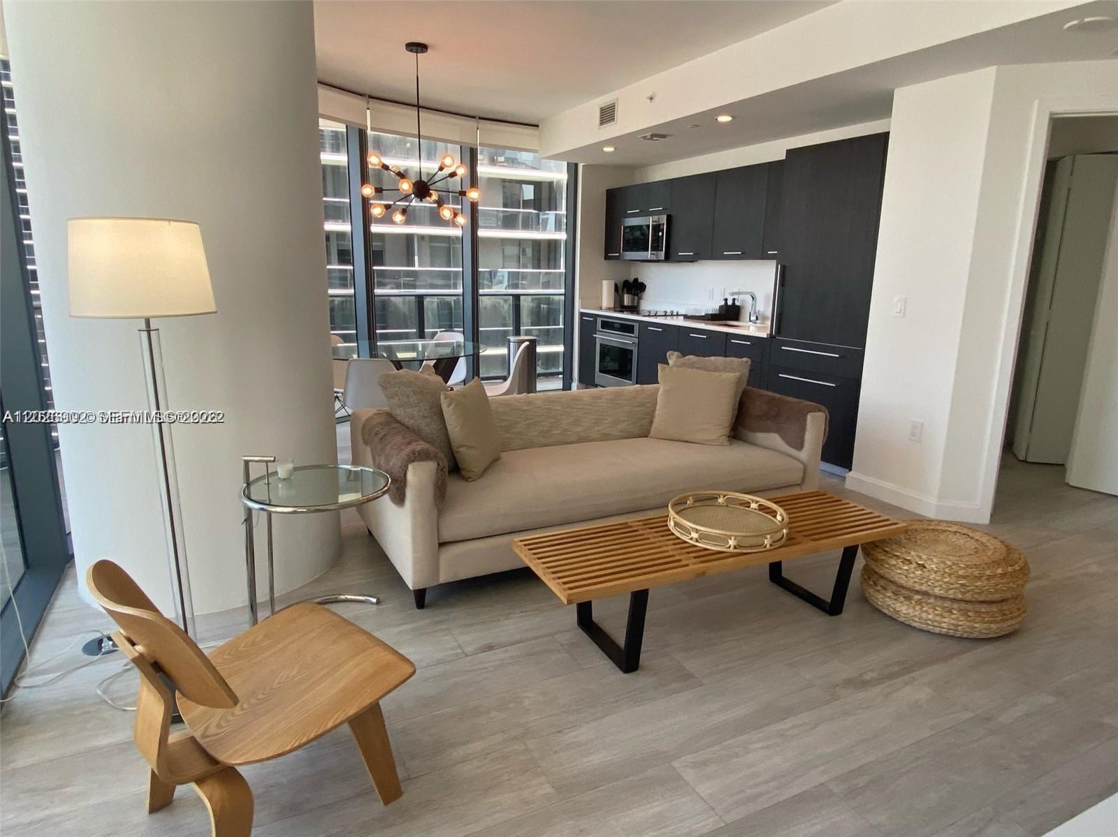 A modern living room features a beige sofa, wooden coffee table, and an open kitchen — 55 SW 9th St # 3001, Miami FL 33130, MIAMI, FL